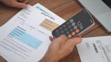 Olgun adam, ev giderlerini hesaplamak için telefon hesap makinesi kullanarak faturaları inceliyor. Muhasebeci, mobil uygulamayı kullanarak yavaş çekim sayımı yapan belgeleri analiz ediyor.