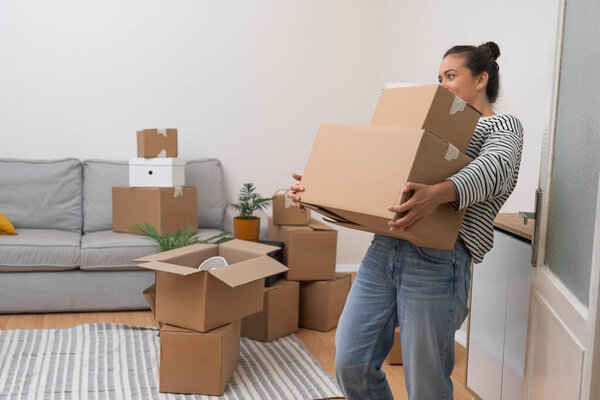 Woman holds heavy boxes with personal items standing in bright premise of new accommodation parcels with things of young lady and transportation concept