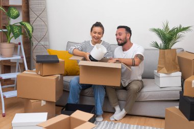 Olumlu yeni evliler, emlakçıdan anahtarları aldıktan sonra karton kutularda toplanan dekorasyonlar arasında yumuşak koltukta birlikte oturarak yeni dairenin satın alınmasını kutluyorlar.