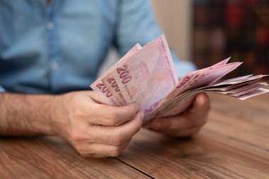 Erkek turist, yüksek enflasyon oranından muzdarip döviz kurunun döviz kuru sonrasında elinde Türk lirası banknotlarıyla bankada oturuyor.