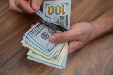 Tahta bir yüzey üzerinde Amerikan doları banknotlarını sayan eller. Nakit işleme ve finansal yönetim kavramı. Kişisel finans, bütçe ve ekonomik işlemler konuları için mükemmel 