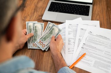 Tahta masadaki vergi belgelerini incelerken para sayan bir adam. Mali yönetim, vergi iadesi ve muhasebe kavramı. 