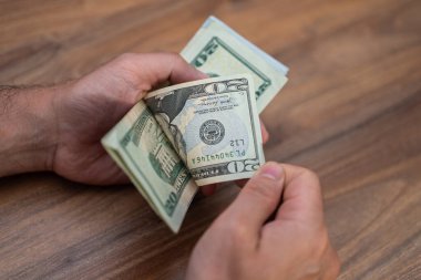 Tahta bir masada el ele tutuşup, dolarları saymak. Nakit işleme ve para yönetimi konsepti. Finans, bütçe ve ekonomik işlemler konuları için ideal 