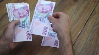 Sanatçı, adil bir tazminat ve artan malzeme maliyetlerini karşılamak için enflasyon arasındaki fiyatlandırma stratejilerini düzenleyen komisyonlardan elde edilen Türk lira banknotlarını saydı