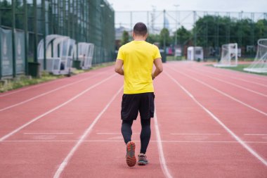 Stadyum boyunca koşan rahat giyimli bir adamın arka planı. Şehir parkındaki çağdaş bir spor sahasında aktif ve sağlıklı bir yaşam tarzı.. 