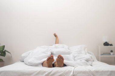 Sabah Esnemesi: Bir kadın yatakta, çıplak ayaklarıyla battaniyeden uzanıyor, neşeli bir şekilde uyanıyor, günü selamlıyor. 