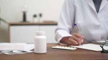 Tıbbi reçete: Yakın çekimde, kadın bir doktor, ultrason görüntüleriyle dolu bir masada otururken hastasına reçete yazar ve titizlikle tıbbi kayıtları doldurur.. 