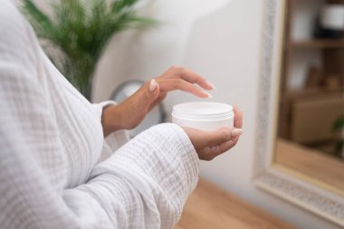 Bir kadın elleri nazikçe banyodaki bir kavanozdan yaşlanma önleyici losyon toplar ve cilt bakımını arttırır.. 