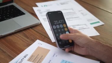 İş adamı faturaları gözden geçirir, toplam telefon miktarından belirli maddeleri çıkartır, yaşlı adam ev maliyesini hesaplar, kağıtları yavaş çekimde analiz eder.