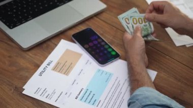 Orta yaşlı işadamı, telefonda hesaplanan faturalarla dolar banknotlarını karşılaştırıyor. Erkek muhasebeci, mali işlemlerin yavaş ilerlemesini sağlıyor.