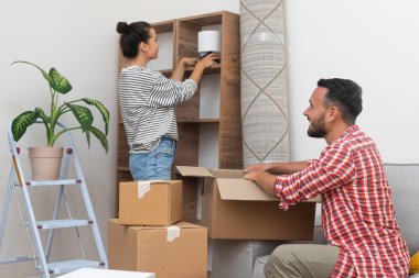 husband and wife, brings warmth to their new home by placing a lamp on an empty shelf, signifying their successful move clipart