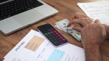 Erkek muhasebeci, telefon hesap makinesine dolar banknotları koyuyor. Tedbirli iş adamı maaştan tasarruf edip ev kontrollerini yavaş çekimde yapıyor.