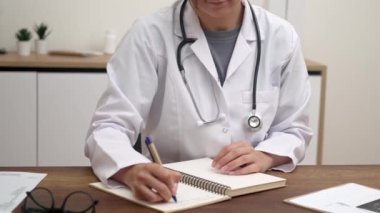 Steteskoplu kadın doktor hasta testlerinin sonuçlarını muayene ediyor. Masada oturup tıbbi rapor yazıyor.