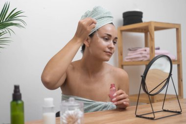 Sakin güzellik: Kafası havluya sarılı bir kadın, aynalı masada rahatlatıcı cilt bakımı için hyaluronik asit serumu kullanır.. 