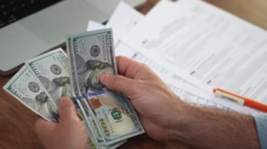 Erkek muhasebeci, ofis harcamalarıyla ilgili vergi belgelerini doldurmak için titizlikle dolar destelerini sayıyor.