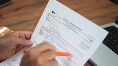 Ofis çalışanı W-4 vergi beyannamesini elinde tutuyor. Belge sahibinin paragraflarını dikkatle okuyor. İş yerini avro banknotları ve dizüstü bilgisayarla ağır çekimde düzenliyor.