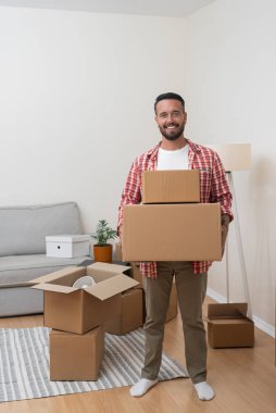 Yeni eve hoş geldiniz. Yeni edinilmiş dairesinde, genç bir beyaz adam, oturma odasına yerleşen bir yığın karton kutu taşıyor.