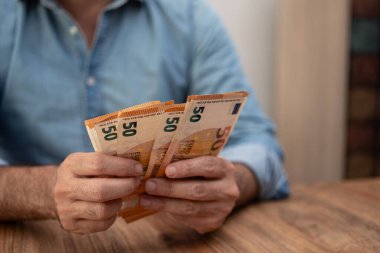 İki elinde de 50 avroluk banknotlar tutan adam ahşap bir masanın üzerinde. Nakit işleme, tasarruf ve kişisel finansmanı vurgulayan mali konsept 