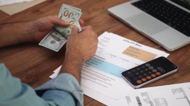 Tişörtlü yaşlı adam masa başına sayılan dolarları dizüstü bilgisayara koyar, erkek muhasebeci faturaları kontrol eder ve ağır çekimde ödeme için para ayırır.