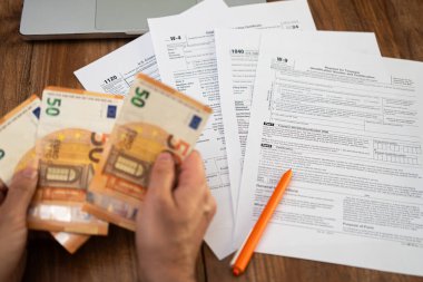 Avro banknotlarını vergi formları ve ahşap bir masada dizüstü bilgisayarı olan bir adamın yakın çekimi. Vergi ödemesi ve finansal organizasyon konsepti. Vergi sezonu ve muhasebe görselleri için uygun 
