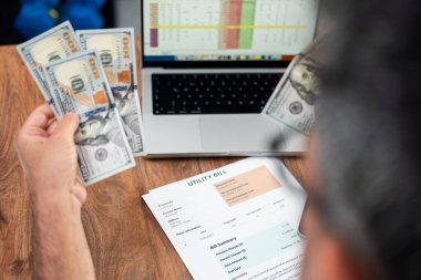 Masadaki faturayı incelerken elinde dolar banknotları tutan gözlüklü bir adamın yakın çekimi. Finansal planlama ve ev bütçesi yönetimi. Ev finansmanı ve ödeme hesapları 
