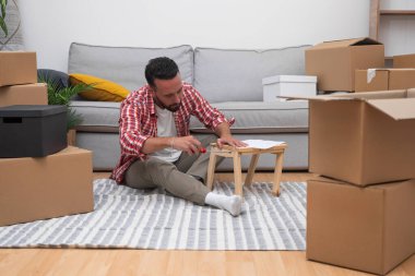 Genç bir adam, kutuları taşıyarak DIY rafını bir araya getiriyor. Yeni evinin yerini değiştirdikten sonra becerilerini sergiliyor.