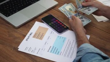 Kıdemli girişimci telefonda finansal faturaları sayan yığınla dolar düzenler, odaklanmış adam elektrik faturaları için nakit ağır çekimde ödeme yapmaya hazırlanır.