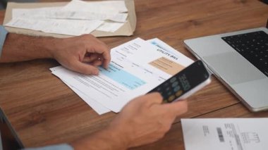 Orta yaşlı erkek ofis çalışanı toplam giderleri ekleyen birden fazla kamu hizmeti faturasını hesaplıyor, erkek muhasebeci şirket ev harcamalarını yavaş çekimde belgeleyen raporlar hazırlıyor