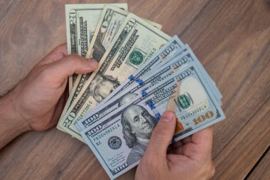 Mevsimlik erkek çalışanın elinde çeşitli dolar banknotları var. Şirket ofisindeki ahşap masada oturarak iş sözleşmesinden sonra maaşı gözden geçiriyorlar.