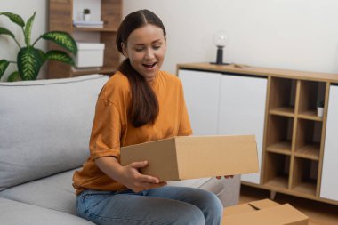 Çevrimiçi Alışveriş Mutluluğu: Kanepesinde dinlenen bir kadın, çevrimiçi alışveriş kolaylığının bir göstergesi olarak teslimatını memnuniyetle alıyor. 