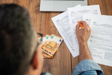 Erkek muhasebeci, işyerindeki devletin avro faturaları ve ofiste dizüstü bilgisayarı olan cezalarından kaçınmak için işletmelerin çeşitli vergi formlarını inceliyor.
