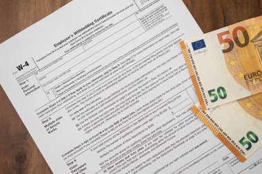 Şirket masasında Euro banknotları bulunan zorunlu W-4 formu, işçilerin işverenin cezadan kaçınmak için yasalara uyma tercihlerini belirtmesi için elzem.