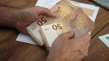 Yaşlı muhasebeci, banknotların her birini tek tek inceleyen avroluk banknotları sayıyor ve masrafları ağır çekimde ödemeye hazırlanıyor.
