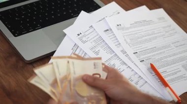 İş sahibi 50 avroluk faturaları hesaplayarak ve şirketle ilgili vergi belgelerini inceleyerek hesapları dengeliyor, adam banknotları ağır çekimde yığına çeviriyor