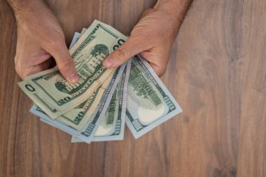 Erkek girişimci elinde dolar banknotları tutarak ayın sonunda şirket ofisindeki işyerinde oturup pahalı faturaları ödemek için para hazırlıyor.