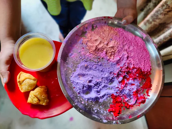 Holi Festivali için kullanılan tepside organik gulal renkleri ve gujiya tutan bir kişinin resmi. Gujiya geleneksel Hint yemeğidir.