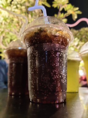 Buzlu kola. Bardakta buz küpleri ve açık havada samanla çekilmiş taze soğuk bir içecek.