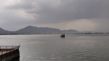 Yağmurlu bir günde gökyüzünde gri bulutlar ve arka planda tepeler olan bir su kütlesinin hızlandırılmış görüntüleri. Ajmer 'de Ana Sagar Gölü' nün manzara görüntüsü.