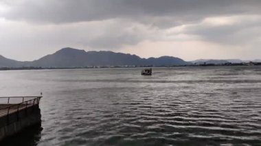 Yağmurlu bir günde gökyüzünde gri bulutlar ve arka planda tepeler olan bir su kütlesinin hızlandırılmış görüntüleri. Ajmer 'de Ana Sagar Gölü' nün manzara görüntüsü.