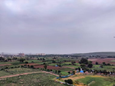 Şehir manzarasının havadan görüntüsü. Arkaplanda bulutlu gökyüzüne karşı tarım arazisi ve binalar