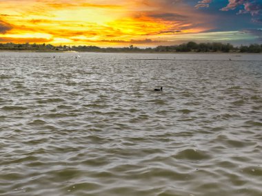 Bulutlu gökyüzü ile gölün üzerinde güzel bir günbatımı resmi. Doğa bileşimi.