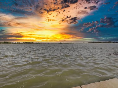 Bulutlu gökyüzü ile gölün üzerinde güzel bir günbatımı resmi. Doğa bileşimi.