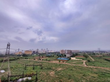 Şehir manzarasının havadan görüntüsü. Arkaplanda bulutlu gökyüzüne karşı tarım arazisi ve binalar