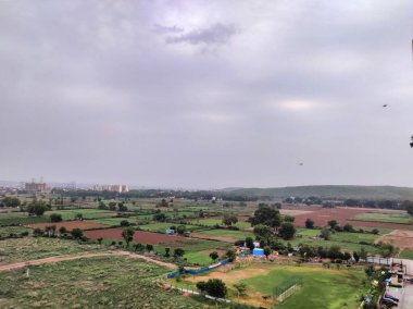 Şehir manzarasının havadan görüntüsü. Arkaplanda bulutlu gökyüzüne karşı tarım arazisi ve binalar