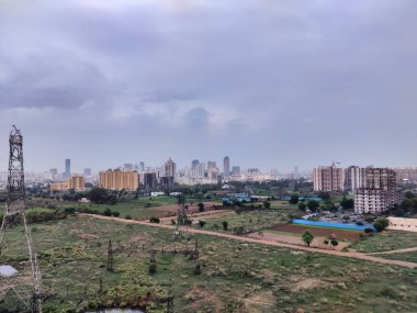 Şehir manzarasının havadan görüntüsü. Arkaplanda bulutlu gökyüzüne karşı tarım arazisi ve binalar