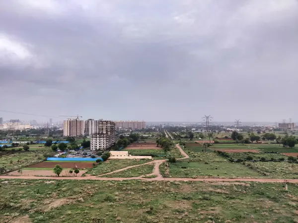 Şehir manzarasının havadan görüntüsü. Arkaplanda bulutlu gökyüzüne karşı tarım arazisi ve binalar