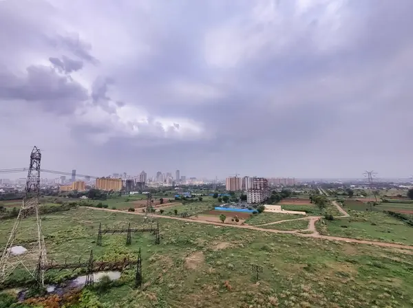 Şehir manzarasının havadan görüntüsü. Arkaplanda bulutlu gökyüzüne karşı tarım arazisi ve binalar