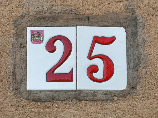 25-25 yaşlarında, beyaz plakalı, İspanya 'nın eski duvarında kırmızı ev numarası yazılı. Arapça rakamlar: iki ve beş. Geleneksel İspanyolca seramik fayans işareti Azulejo.