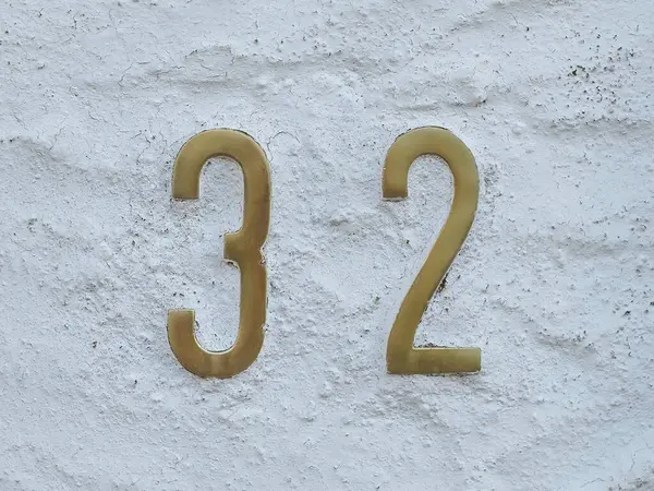 32 ya da 32, altın sarısı ev numarası sokakta. Arapça rakamlar: üç ve iki. Eski alçılı duvar arkaplanındaki geleneksel rakamlar, kapatın.