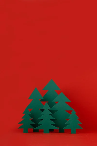 stock image Christmas funny childish background with paper green spruce forest on saturated festive red backdrop in modern minimalist style, copy space, vertical. New year season mockup for design, greeting card.